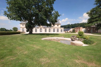 Petit pont en pierre surplombant un chemin, entouré de verdure et jouxtant un bâtiment ancien avec toiture en ardoise.
