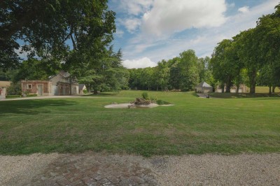 Petit pont en pierre surplombant un chemin, entouré de verdure et jouxtant un bâtiment ancien avec toiture en ardoise.