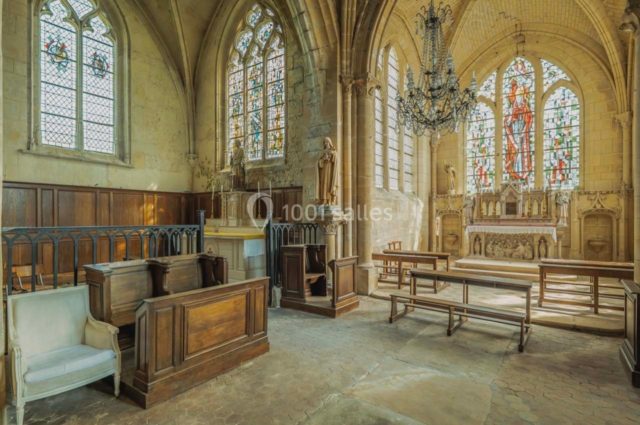 Intérieur d'une église avec bancs en bois, autel décoré, vitraux colorés et lustre suspendu.