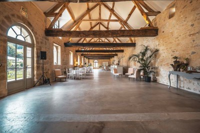 Petit pont en pierre surplombant un chemin, entouré de verdure et jouxtant un bâtiment ancien avec toiture en ardoise.