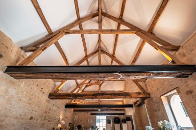 Petit pont en pierre surplombant un chemin, entouré de verdure et jouxtant un bâtiment ancien avec toiture en ardoise.