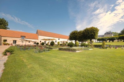 Petit pont en pierre surplombant un chemin, entouré de verdure et jouxtant un bâtiment ancien avec toiture en ardoise.