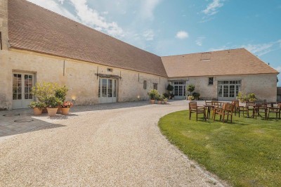 Petit pont en pierre surplombant un chemin, entouré de verdure et jouxtant un bâtiment ancien avec toiture en ardoise.