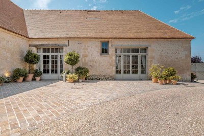 Petit pont en pierre surplombant un chemin, entouré de verdure et jouxtant un bâtiment ancien avec toiture en ardoise.