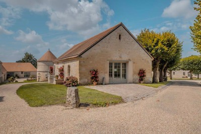 Petit pont en pierre surplombant un chemin, entouré de verdure et jouxtant un bâtiment ancien avec toiture en ardoise.
