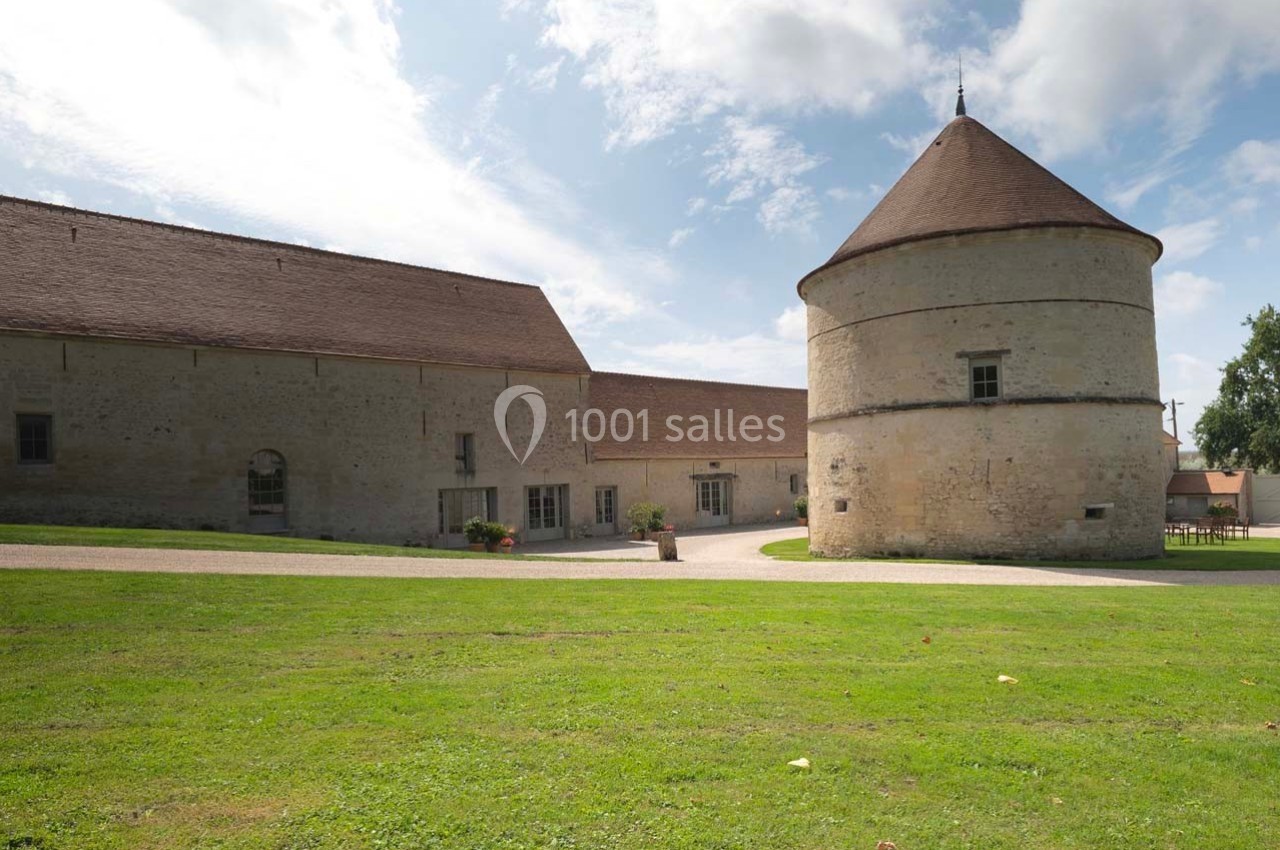 Bâtiments anciens en pierre avec une tour ronde et un toit en tuiles, entourés d'une pelouse sous un ciel partiellement…