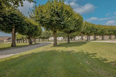 Petit pont en pierre surplombant un chemin, entouré de verdure et jouxtant un bâtiment ancien avec toiture en ardoise.