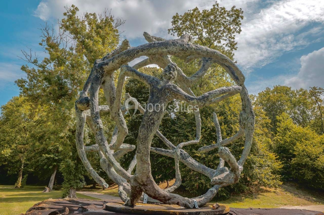Sculpture en métal représentant une sphère formée de branches entrelacées, exposée dans un parc verdoyant.
