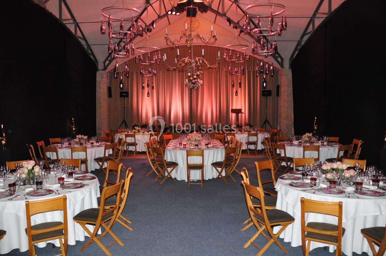 Salle de réception décorée avec des tables rondes dressées, éclairage tamisé et lustres suspendus.
