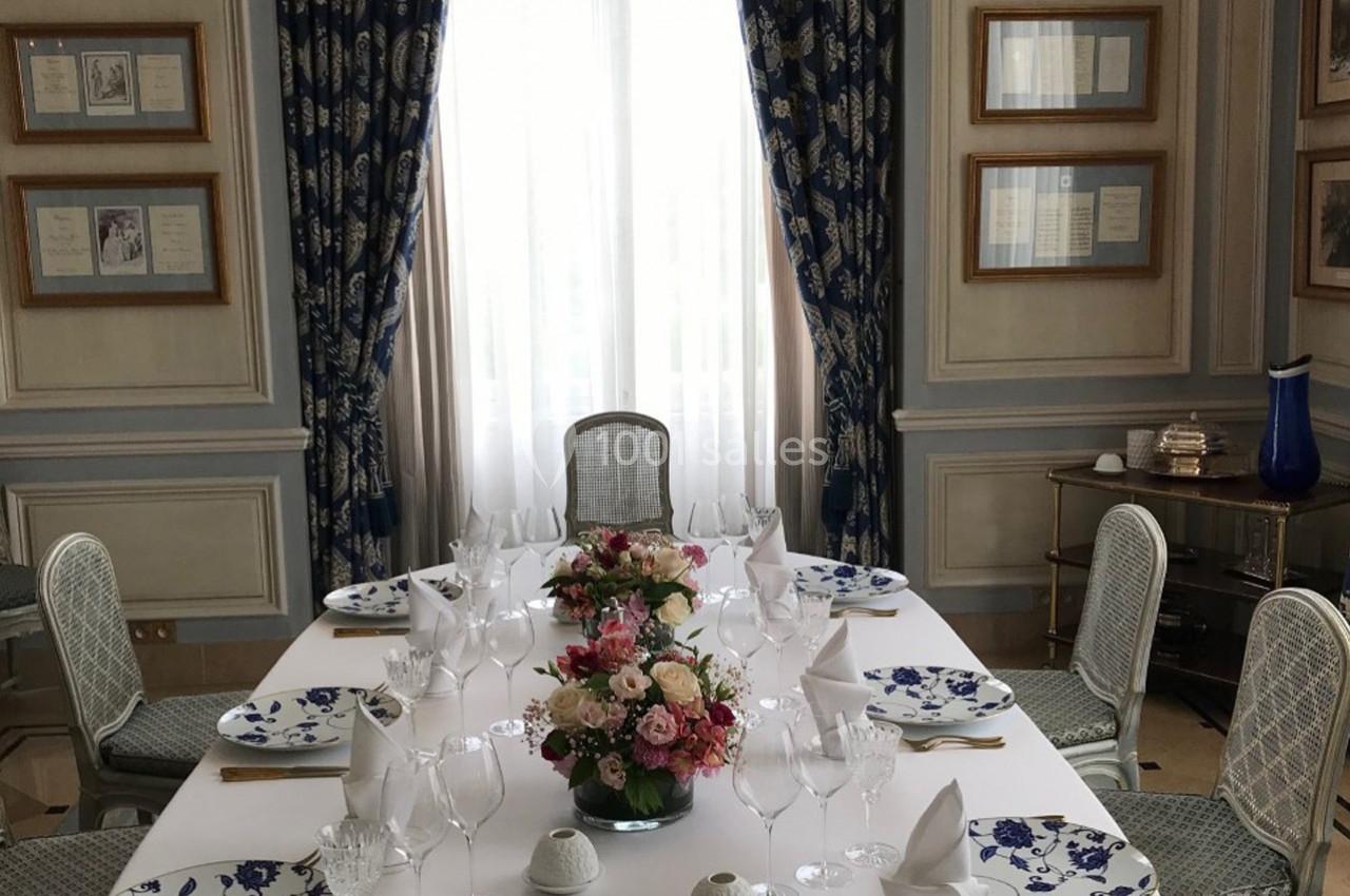 Table élégamment dressée avec vaisselle à motifs bleus, bouquet de fleurs au centre, dans une salle lumineuse et raffinée.