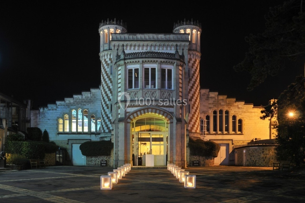 Façade illuminée d'un bâtiment historique en pierre, de style château, avec des lanternes alignées au sol.