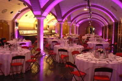 Salle voûtée décorée avec des tables rondes dressées pour un événement, éclairée par des lumières violettes.