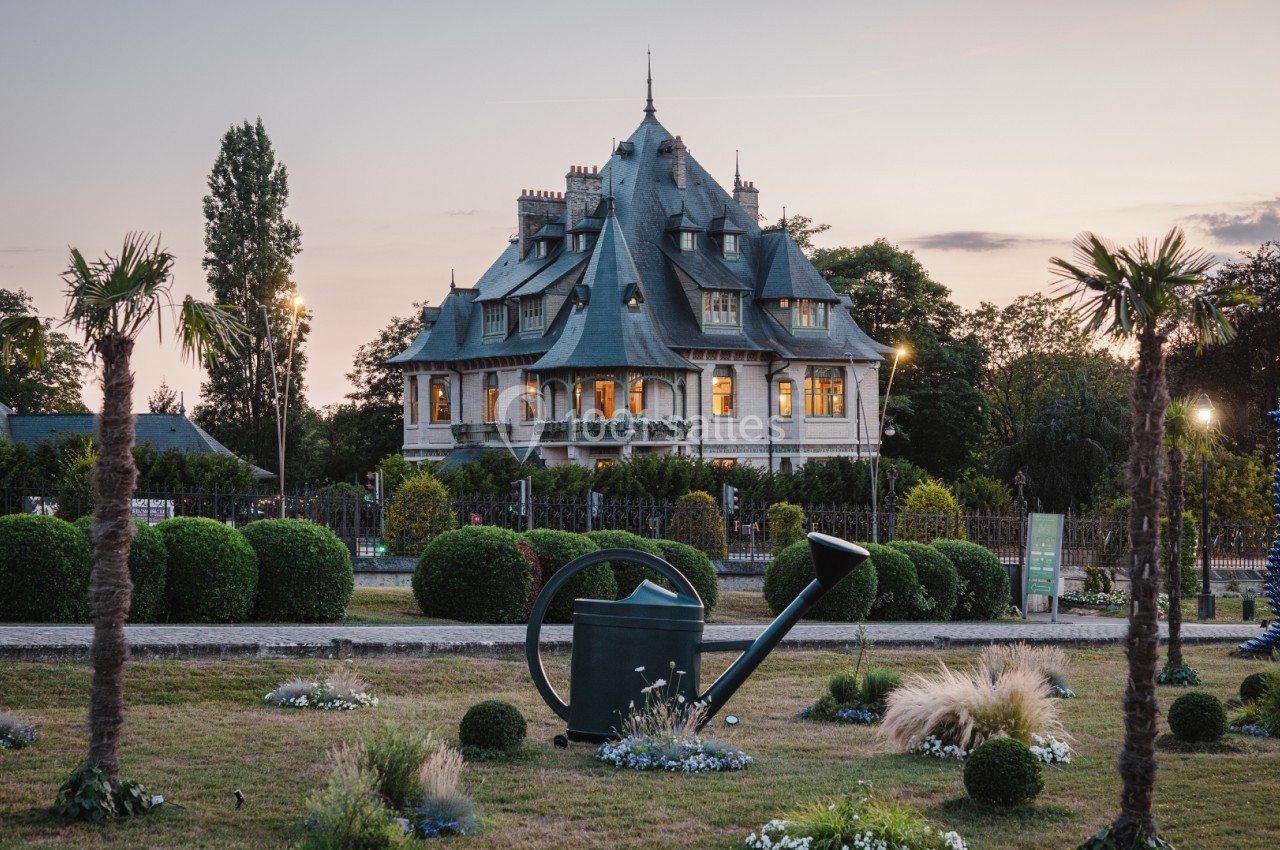 Manoir entouré d'un jardin paysager avec sculptures, palmiers et éclairage au crépuscule.
