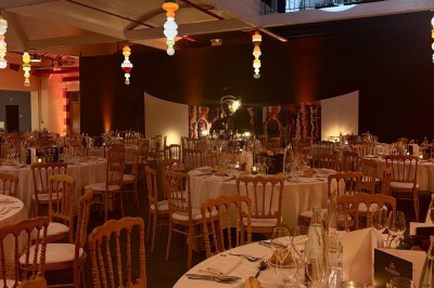 Salle voûtée décorée avec des tables rondes dressées pour un événement, éclairée par des lumières violettes.