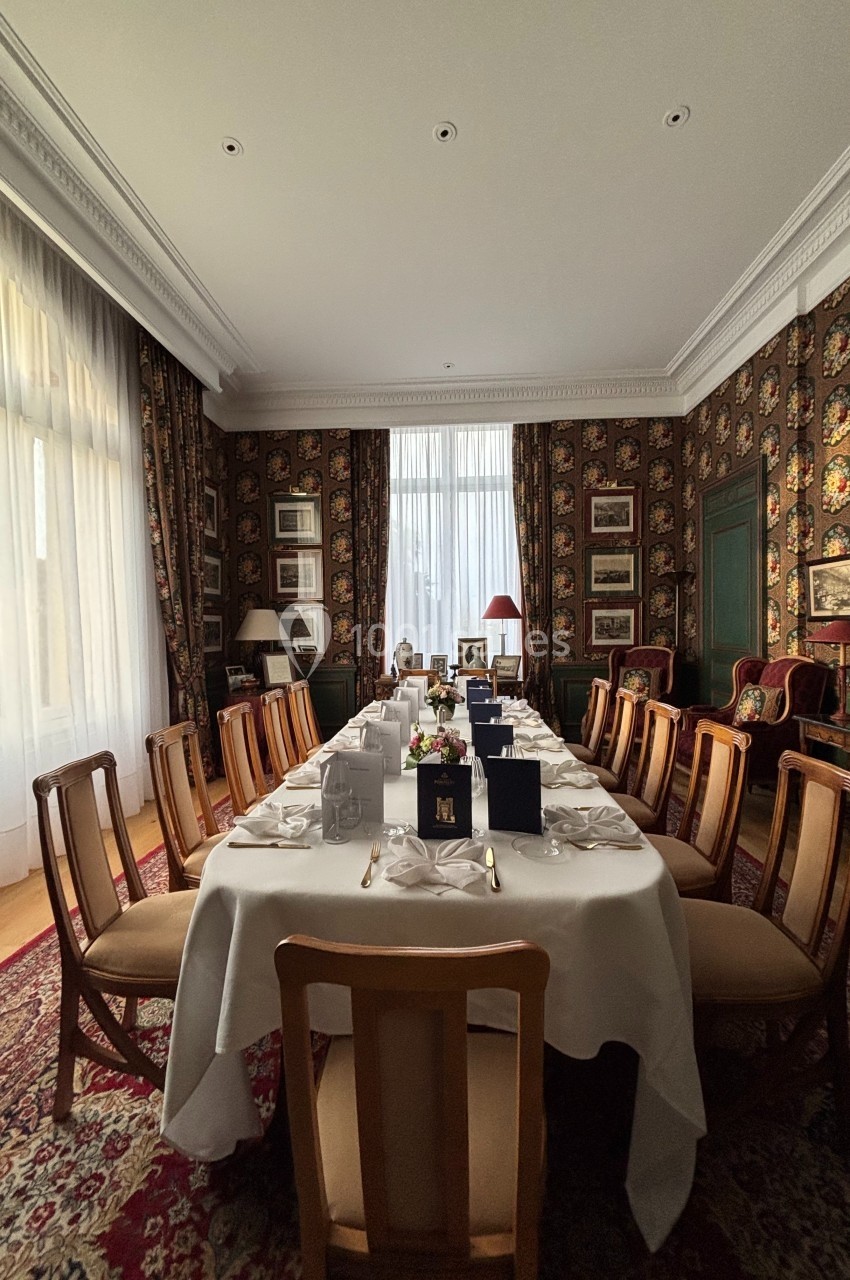 Salle à manger élégante avec une grande table dressée, entourée de chaises en bois, dans un décor classique et chaleureux.