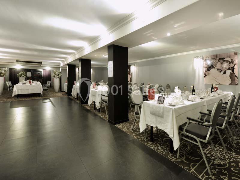 Salle de réception élégante avec tables dressées, nappes blanches et chaises grises, éclairage doux et décor raffiné.