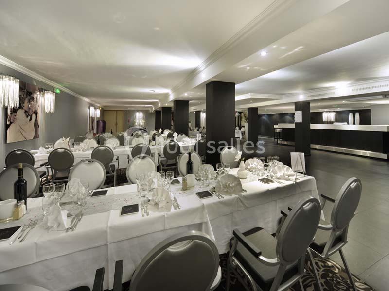 Salle de réception élégante avec tables dressées, nappes blanches, chaises grises et éclairage moderne.