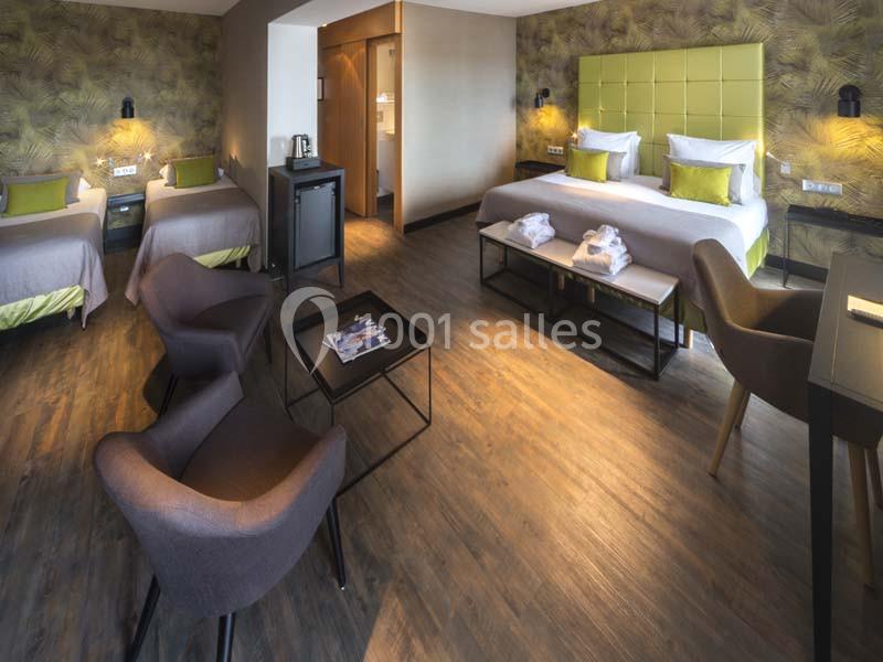 Chambre d'hôtel spacieuse avec deux lits simples, un lit double, coin salon, parquet et décoration moderne.