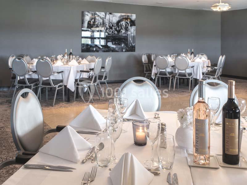 Salle de restaurant élégante avec tables dressées, nappes blanches, verres, bouteilles de vin et éclairage tamisé.