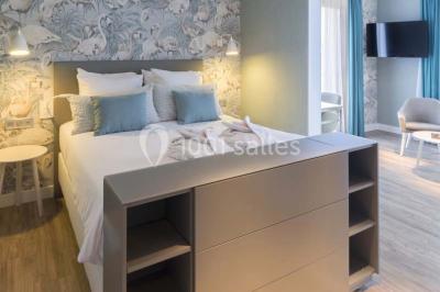 Chambre lumineuse avec lit double, papier peint à motifs de flamants roses, mobilier moderne et télévision murale.