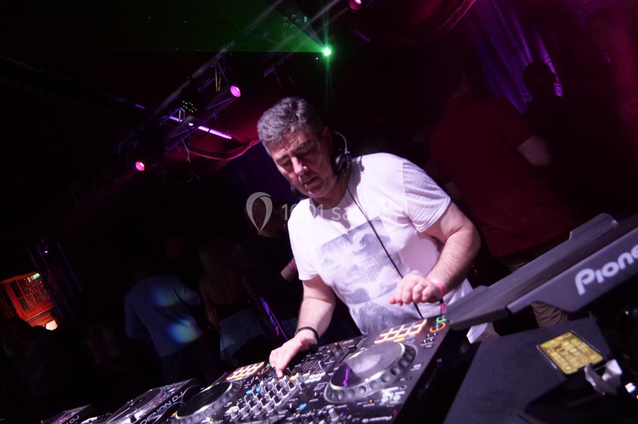 Un DJ mixant de la musique sur une table de mixage dans une ambiance de soirée avec éclairages colorés.