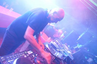 Un DJ mixe sur scène dans une ambiance sombre et lumineuse, décorée avec des éléments d'Halloween.