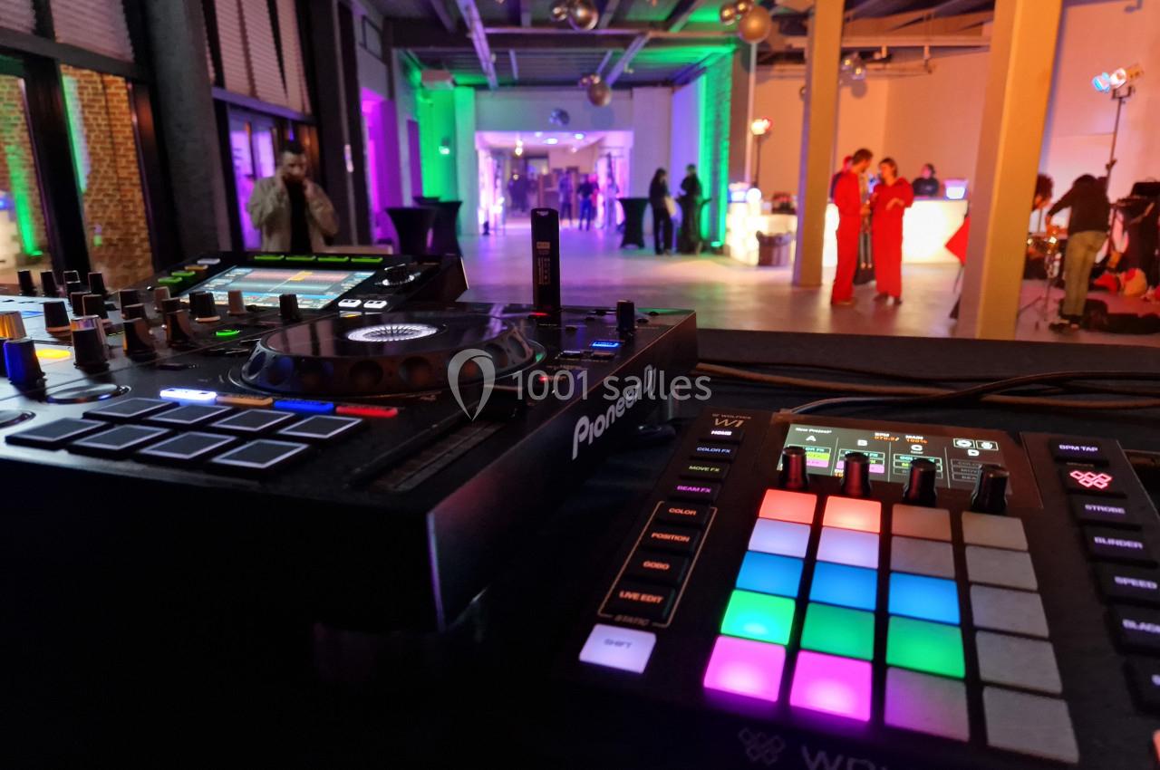 Vue rapprochée d'une console DJ et d'un contrôleur lumineux, avec une salle éclairée en arrière-plan.