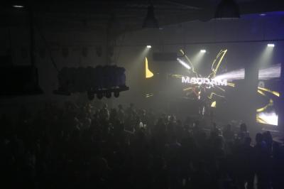 Un DJ mixe sur scène dans une ambiance sombre et lumineuse, décorée avec des éléments d'Halloween.