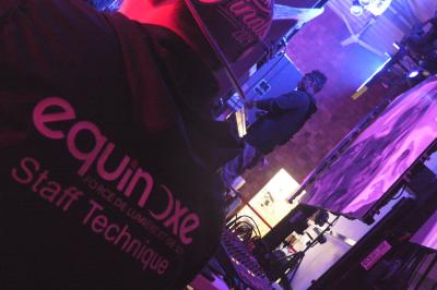 Un DJ mixe sur scène dans une ambiance sombre et lumineuse, décorée avec des éléments d'Halloween.