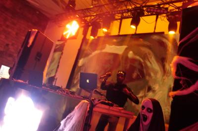 Un DJ mixe sur scène dans une ambiance sombre et lumineuse, décorée avec des éléments d'Halloween.