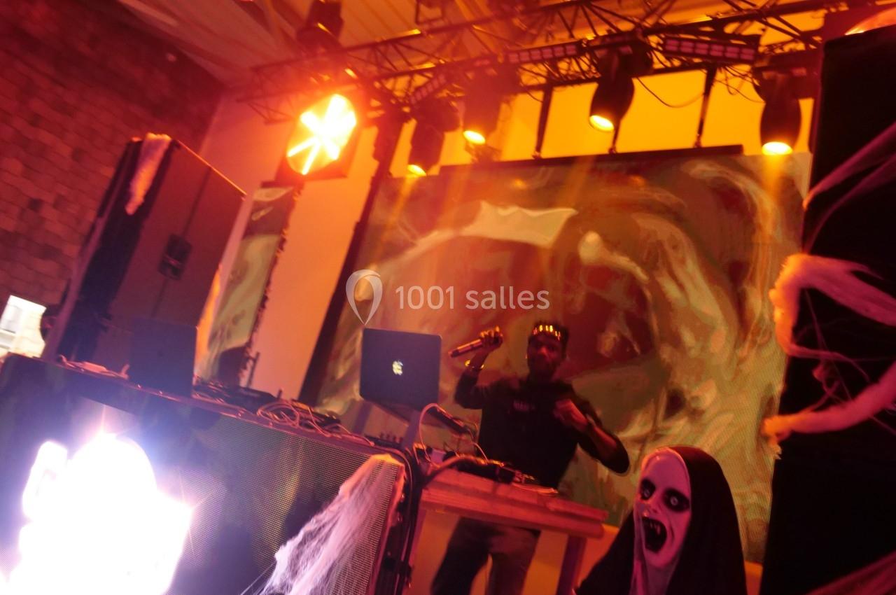 Un DJ mixe sur scène dans une ambiance sombre et lumineuse, décorée avec des éléments d'Halloween.