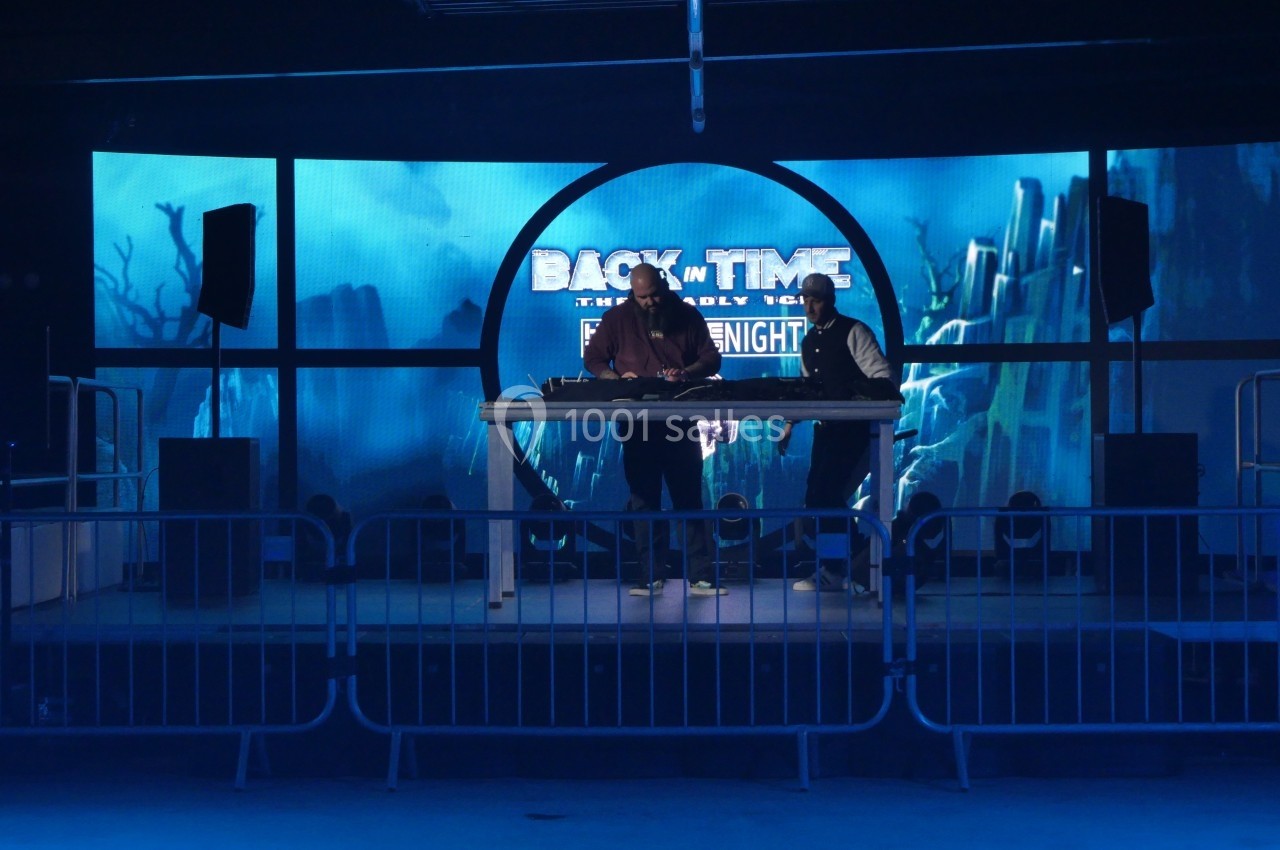 Deux personnes sur une scène avec un écran lumineux en arrière-plan affichant ’Back in Time’.