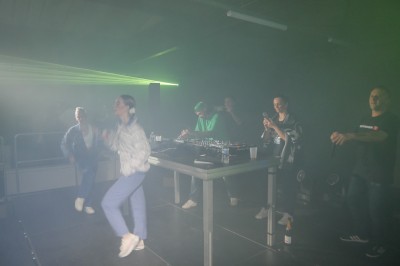 Un DJ mixe sur une scène éclairée, avec un écran lumineux affichant des motifs rouges en arrière-plan.