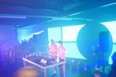 Un DJ mixe sur scène avec des jeux de lumière jaunes et un écran affichant une image de crâne en arrière-plan.