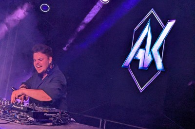 Un DJ mixe sur scène avec des jeux de lumière jaunes et un écran affichant une image de crâne en arrière-plan.