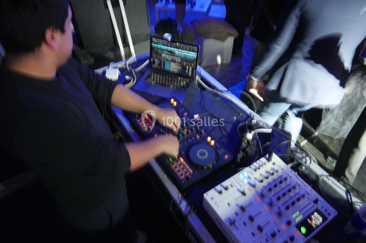 Un DJ mixe de la musique sur une console avec un ordinateur portable dans un environnement éclairé en bleu.