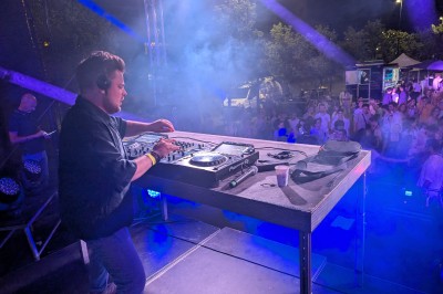 Un homme en t-shirt noir échange avec deux autres personnes près d'une table de mixage dans une salle éclairée par des…
