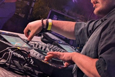 Un homme en t-shirt noir échange avec deux autres personnes près d'une table de mixage dans une salle éclairée par des…