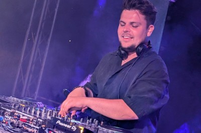 Un homme en t-shirt noir échange avec deux autres personnes près d'une table de mixage dans une salle éclairée par des…
