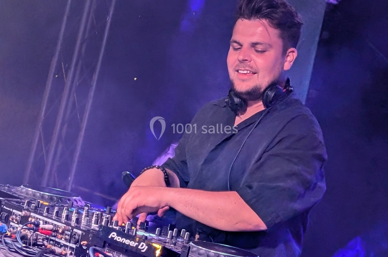 Un DJ souriant mixe de la musique sur une console Pioneer DJ dans une ambiance lumineuse et enfumée.