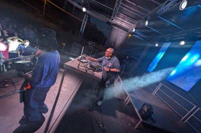 Un homme en t-shirt noir échange avec deux autres personnes près d'une table de mixage dans une salle éclairée par des…