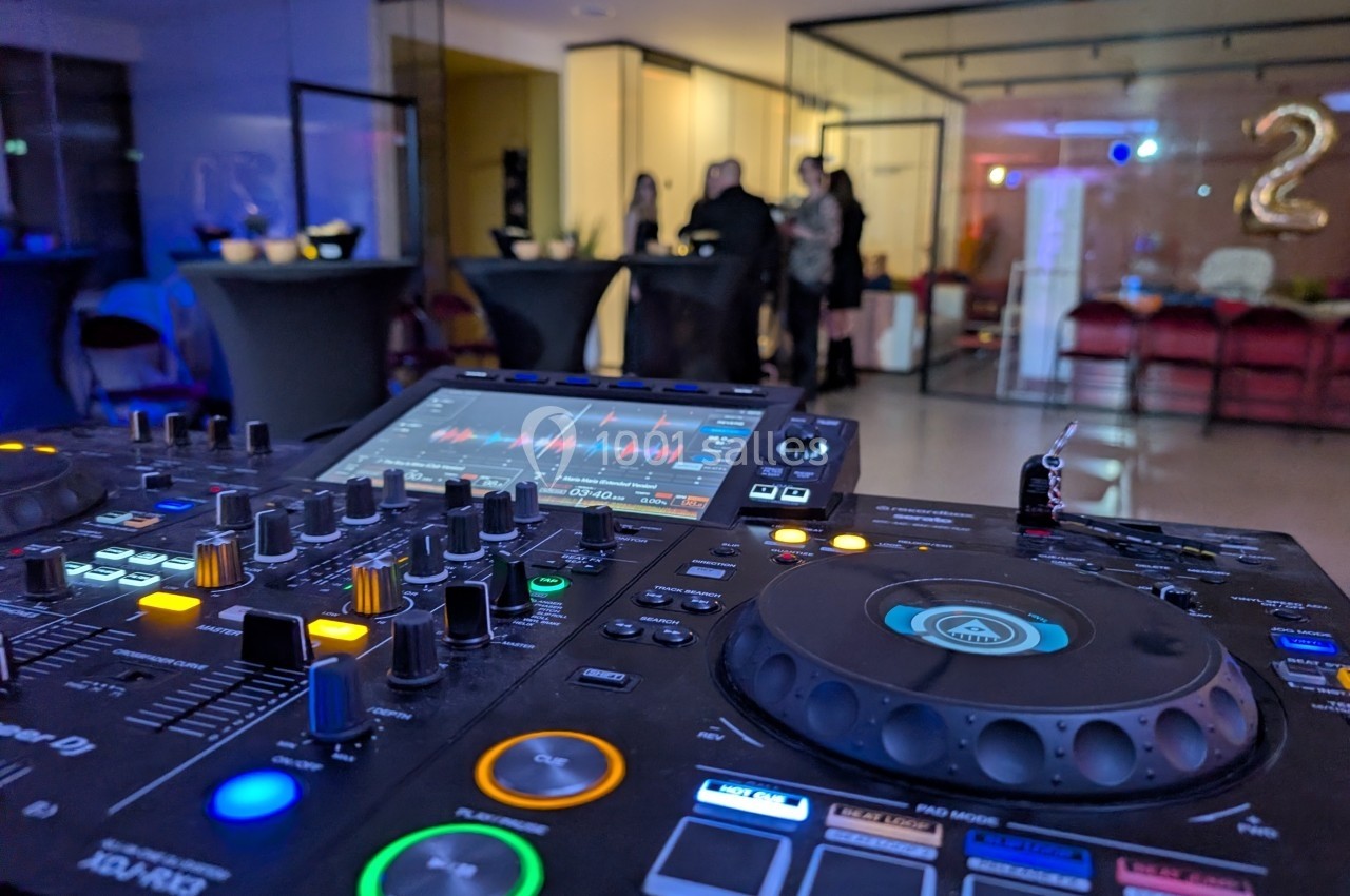 Table de mixage DJ en gros plan avec des invités flous en arrière-plan dans une salle de réception éclairée.