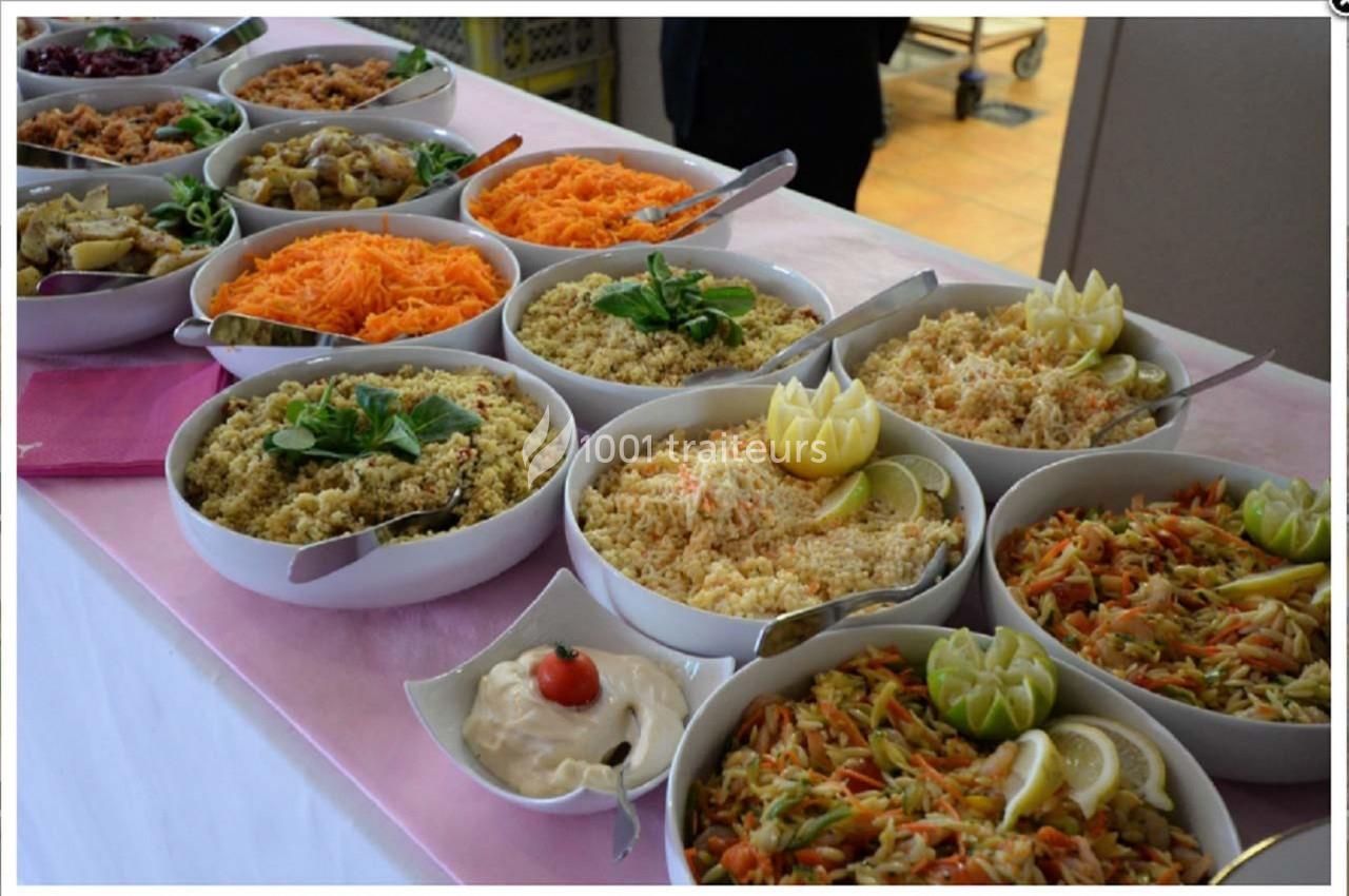 Buffet de salades variées avec carottes râpées, taboulé, légumes, et sauce, présenté dans des bols sur une nappe rose.