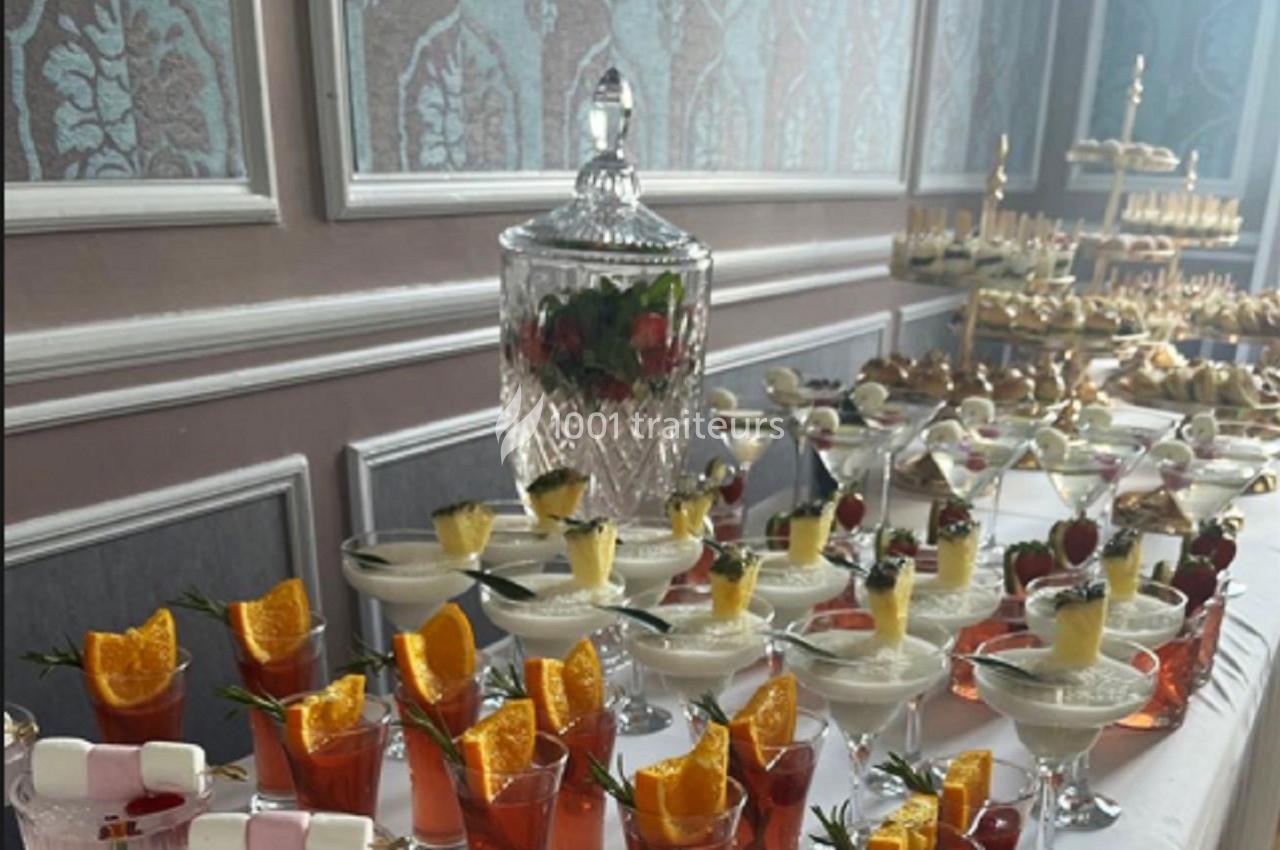 Table garnie de desserts variés, cocktails décorés de fruits et verrines, dans une salle élégante avec moulures.