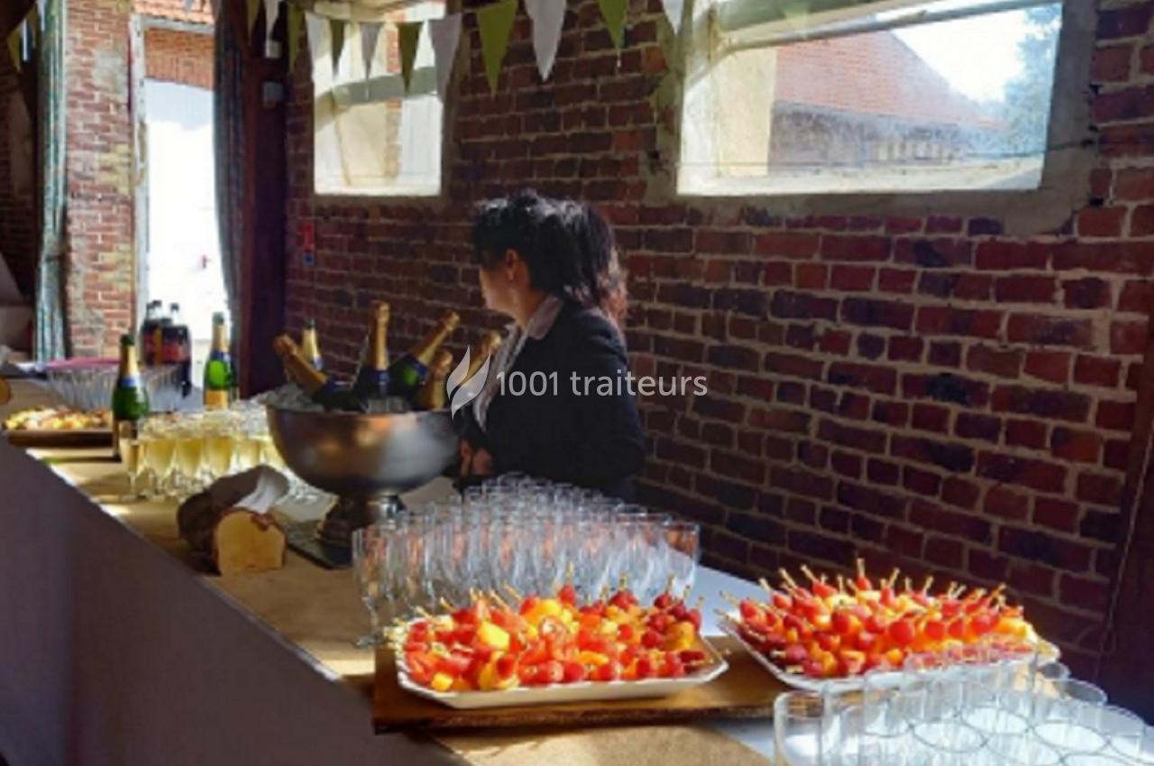 Table de réception avec coupes de champagne, brochettes apéritives et serveuse dans une salle en briques lumineuse.