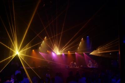 Un bus stationné de nuit devant un bâtiment illuminé, avec des passants en arrière-plan.