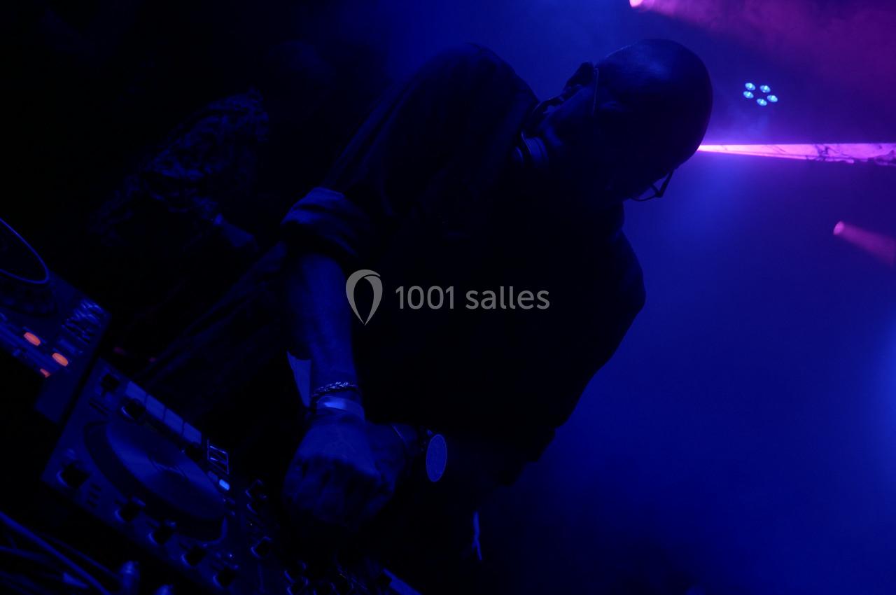 Un DJ mixant de la musique dans une ambiance sombre avec des lumières bleues et violettes.