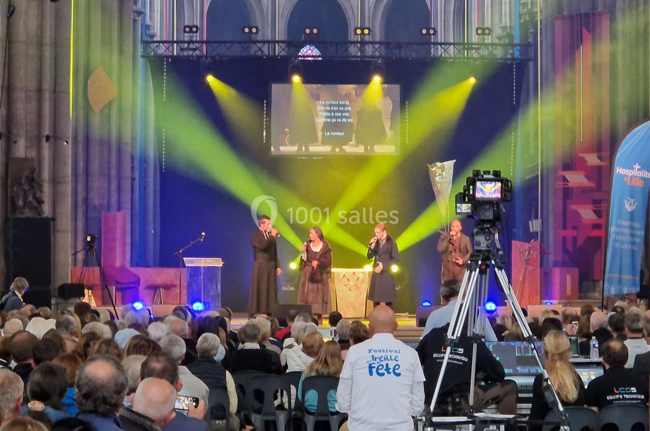 Quatre personnes chantent sur une scène éclairée dans une église, devant un public assis.
