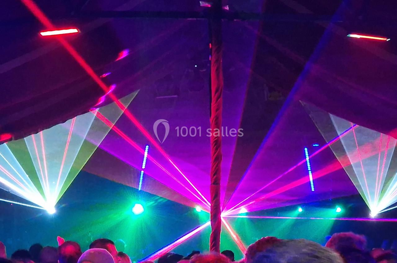 Foule dans une ambiance festive sous une tente, éclairée par des faisceaux lumineux colorés et des lasers.