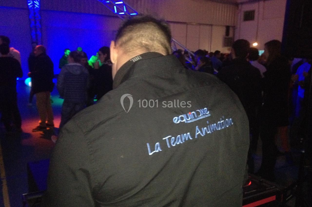 Un animateur de dos portant une chemise avec un logo, dans une salle éclairée par des lumières colorées.